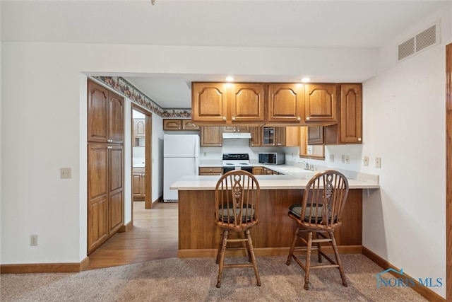 kitchen with kitchen peninsula, a kitchen breakfast bar, light hardwood / wood-style flooring, sink, and white appliances