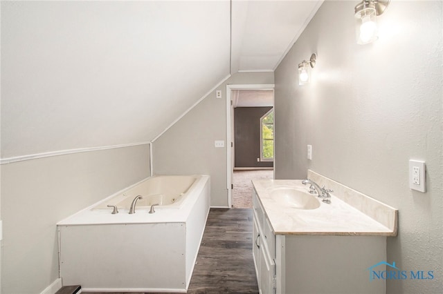 bathroom with hardwood / wood-style flooring, ornamental molding, vaulted ceiling, a bathing tub, and vanity