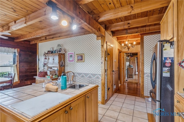 kitchen with sink, stainless steel fridge, tile counters, beam ceiling, and light tile patterned floors