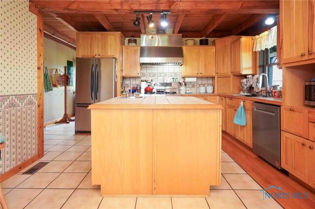 kitchen featuring tile countertops, wood ceiling, wall chimney exhaust hood, a sink, and stainless steel appliances