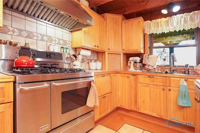 kitchen with range with two ovens, tasteful backsplash, a sink, light countertops, and wall chimney exhaust hood