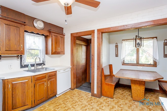 kitchen featuring ceiling fan, white dishwasher, sink, decorative light fixtures, and brick wall