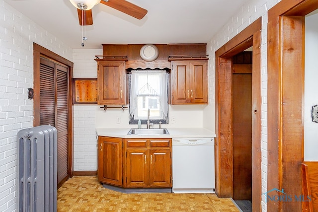 kitchen with radiator heating unit, light parquet flooring, dishwasher, sink, and brick wall