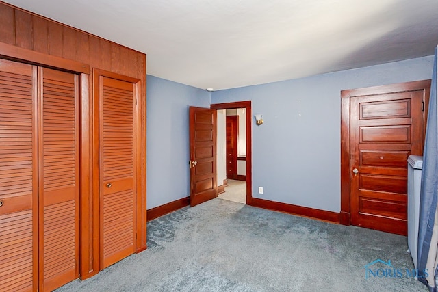 unfurnished bedroom featuring light carpet, a closet, and wood walls