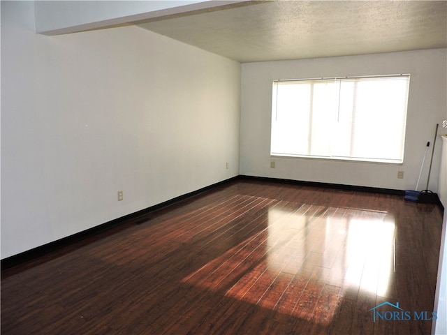 empty room featuring a textured ceiling and dark hardwood / wood-style floors