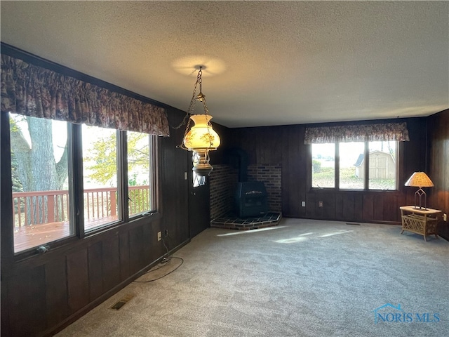 unfurnished dining area featuring a wood stove, carpet floors, a textured ceiling, and wood walls