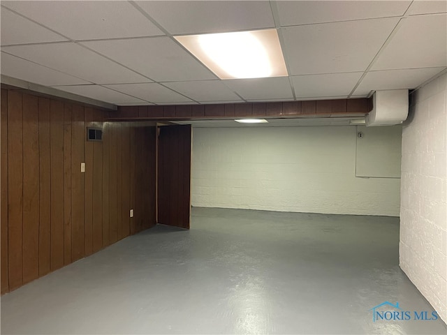 basement featuring a drop ceiling and wooden walls