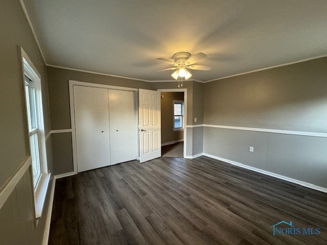 unfurnished bedroom with dark wood-type flooring, crown molding, a closet, and ceiling fan