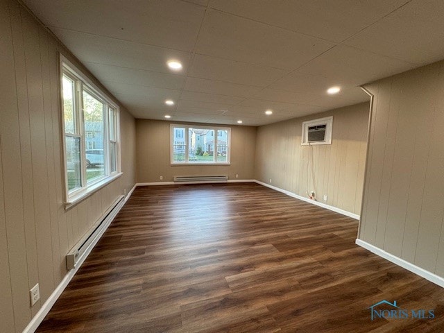 empty room featuring a baseboard radiator, wooden walls, a wall mounted air conditioner, and dark hardwood / wood-style flooring