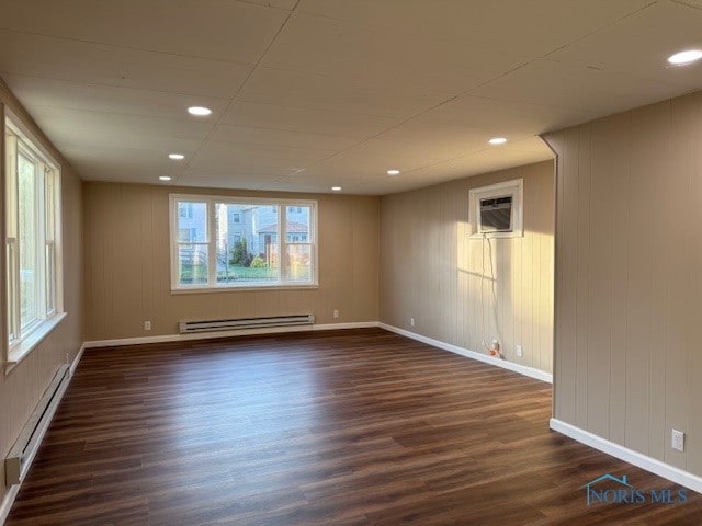 unfurnished room with a baseboard heating unit, plenty of natural light, and dark hardwood / wood-style floors