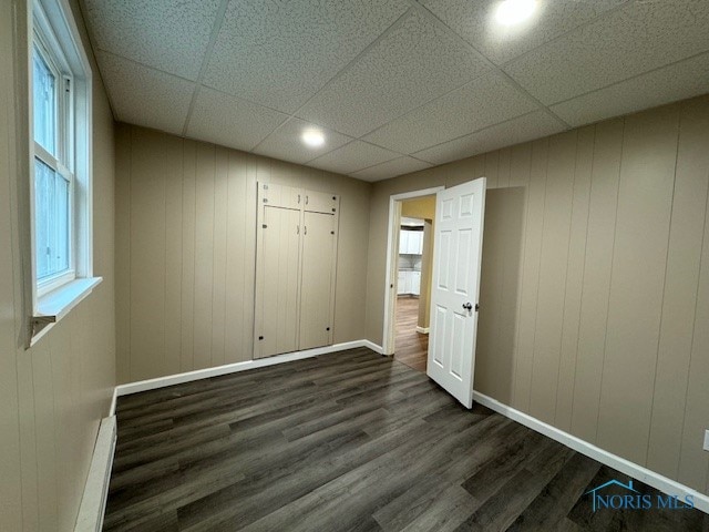 unfurnished bedroom featuring a drop ceiling, a baseboard heating unit, and dark wood-type flooring