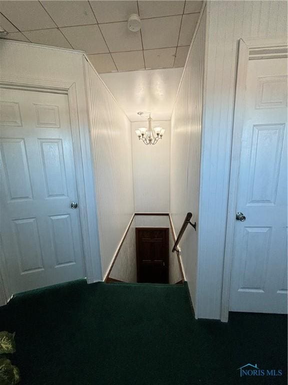 staircase with an inviting chandelier and wood walls