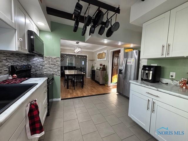 kitchen featuring light tile patterned floors, stainless steel refrigerator with ice dispenser, black electric range, tasteful backsplash, and white cabinets