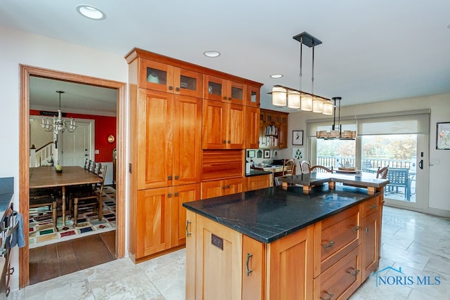 kitchen featuring dark stone counters, pendant lighting, crown molding, a chandelier, and a kitchen island with sink