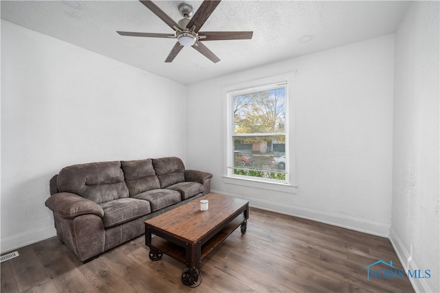 living room with a textured ceiling, ceiling fan, and dark hardwood / wood-style flooring