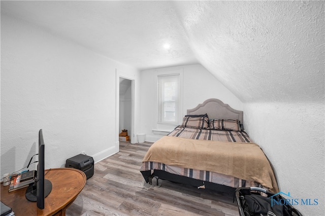 bedroom with a spacious closet, a textured ceiling, wood-type flooring, and lofted ceiling