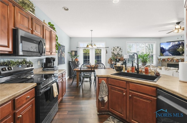 kitchen featuring dark wood-type flooring, hanging light fixtures, sink, black appliances, and ceiling fan with notable chandelier