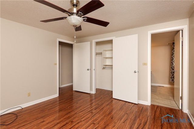 unfurnished bedroom featuring a walk in closet, ceiling fan, a textured ceiling, dark wood-type flooring, and a closet