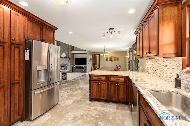 kitchen featuring kitchen peninsula, a brick fireplace, stainless steel appliances, sink, and a notable chandelier