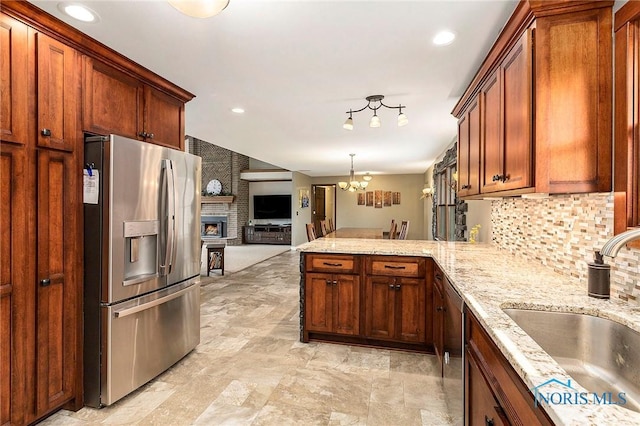 kitchen featuring sink, appliances with stainless steel finishes, tasteful backsplash, a large fireplace, and kitchen peninsula