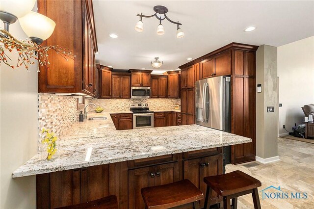 kitchen featuring kitchen peninsula, a kitchen bar, stainless steel appliances, sink, and pendant lighting