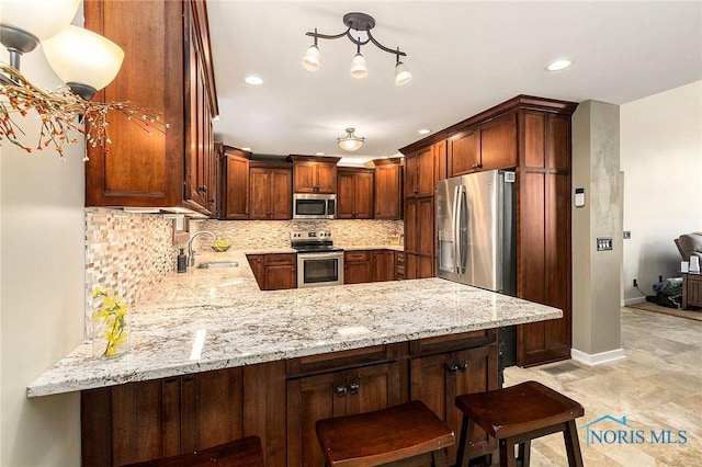 kitchen featuring appliances with stainless steel finishes, pendant lighting, sink, decorative backsplash, and kitchen peninsula