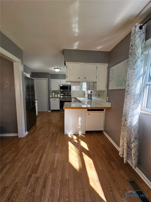 kitchen featuring kitchen peninsula, black stove, dark hardwood / wood-style flooring, sink, and white cabinetry