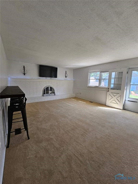 unfurnished living room featuring a tile fireplace, a textured ceiling, and carpet floors