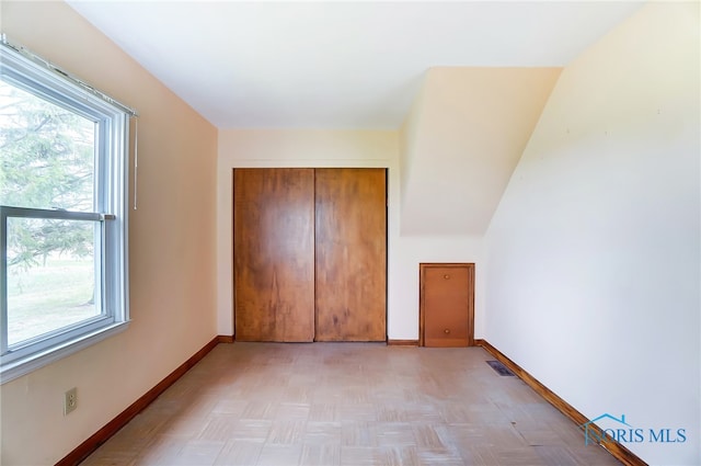 unfurnished bedroom featuring a closet, light parquet floors, and lofted ceiling