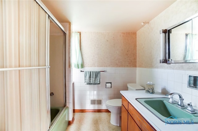 full bathroom featuring tile walls, bath / shower combo with glass door, vanity, and toilet