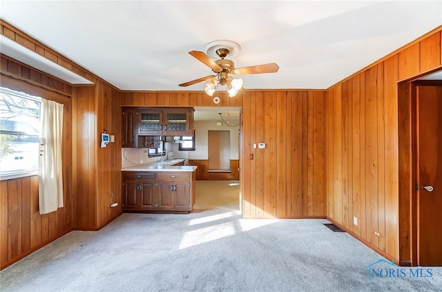 kitchen with wooden walls, sink, light colored carpet, and ceiling fan