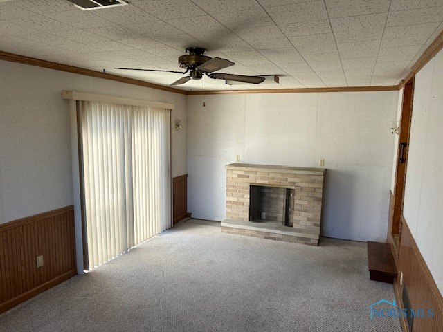 unfurnished living room featuring crown molding, light colored carpet, a fireplace, and ceiling fan