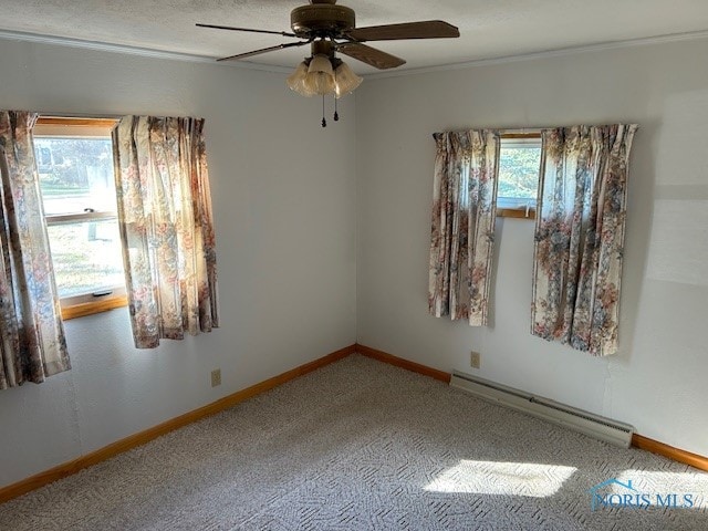 carpeted spare room featuring ceiling fan, ornamental molding, a baseboard heating unit, and plenty of natural light