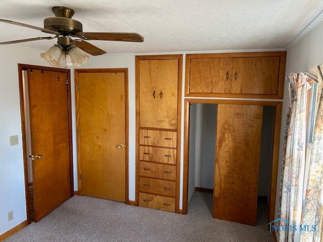 unfurnished bedroom featuring a textured ceiling, ornamental molding, light colored carpet, and ceiling fan