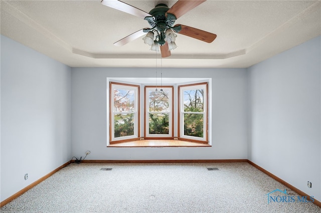 carpeted empty room with a textured ceiling, a tray ceiling, and ceiling fan