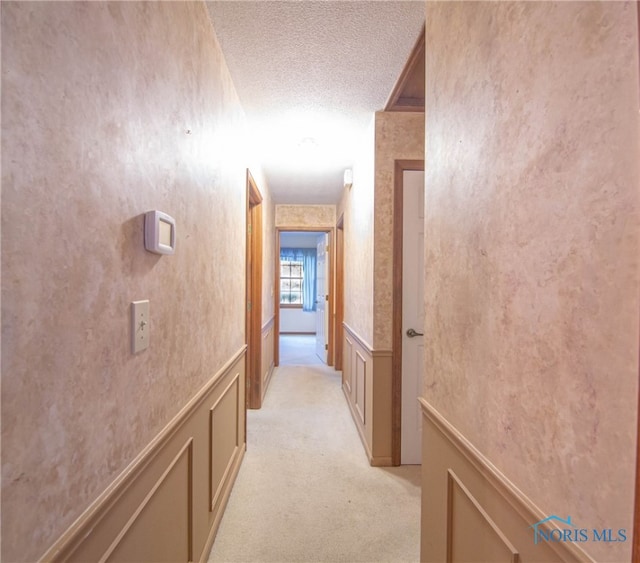 hall with a textured ceiling and light colored carpet