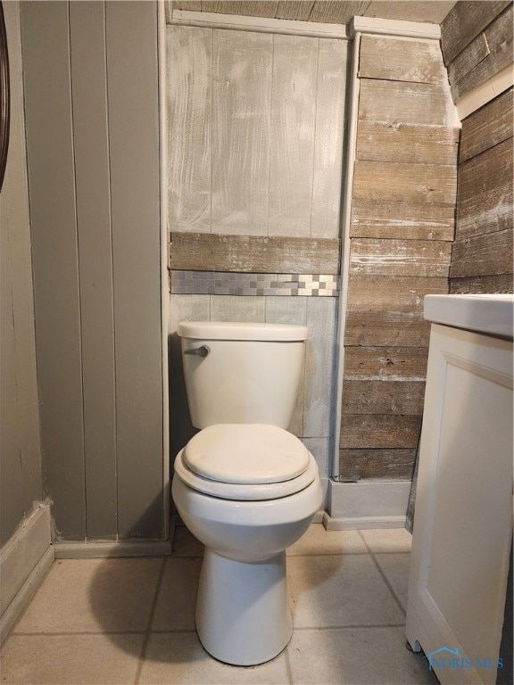 bathroom with toilet, vanity, wooden walls, and tile patterned flooring