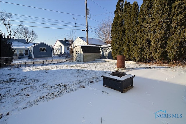 snowy yard featuring a storage shed and an outdoor fire pit