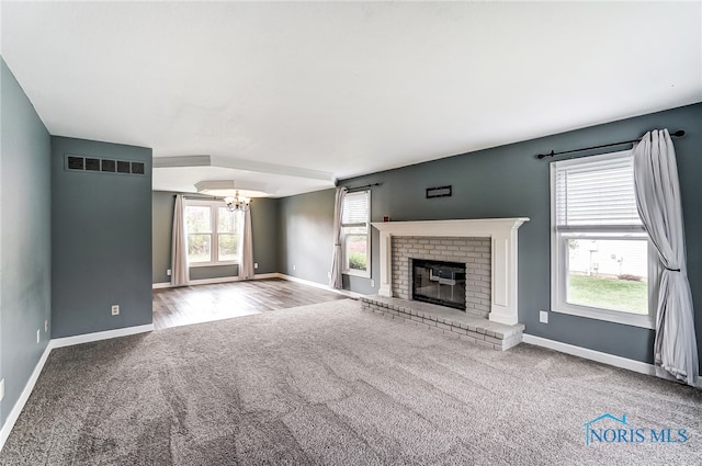 unfurnished living room with a brick fireplace, hardwood / wood-style floors, and a notable chandelier