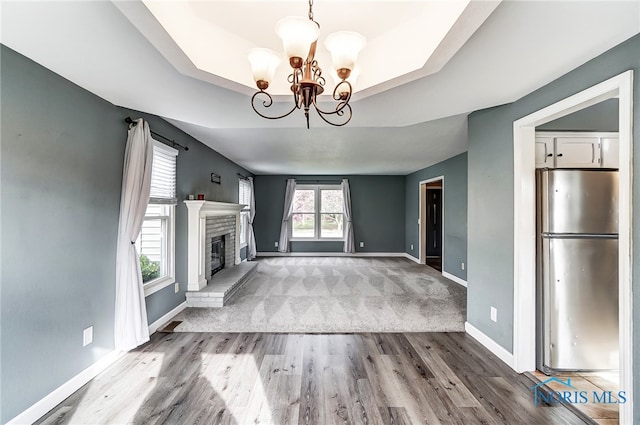 unfurnished living room featuring a brick fireplace, hardwood / wood-style flooring, a raised ceiling, and a notable chandelier