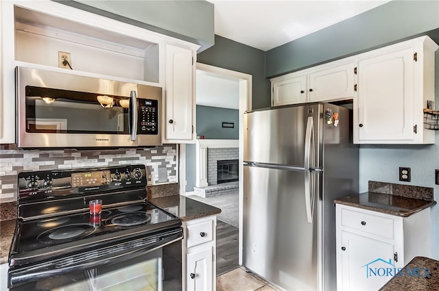 kitchen with white cabinets, dark stone countertops, a fireplace, and appliances with stainless steel finishes