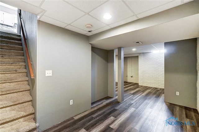 basement with dark hardwood / wood-style flooring, a paneled ceiling, and brick wall