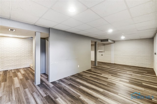 basement featuring dark hardwood / wood-style floors, a paneled ceiling, and brick wall