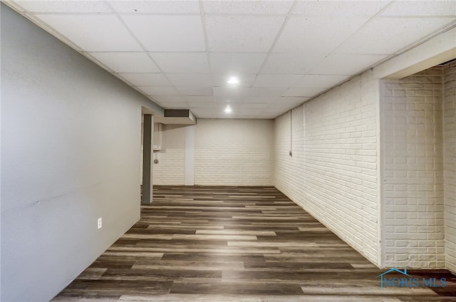 basement with a paneled ceiling, dark hardwood / wood-style floors, and brick wall