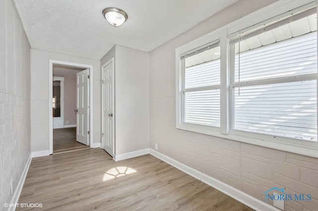 unfurnished room featuring a textured ceiling, light hardwood / wood-style floors, and brick wall