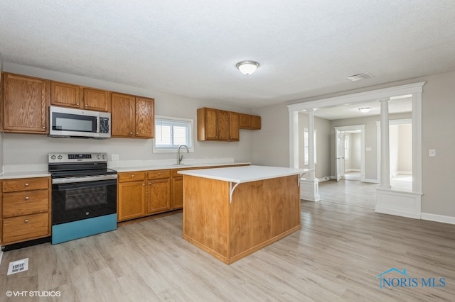 kitchen featuring sink, appliances with stainless steel finishes, light hardwood / wood-style flooring, decorative columns, and a center island