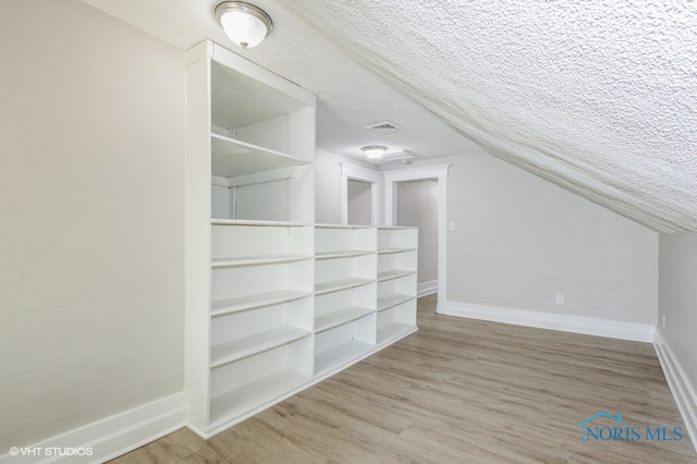 additional living space featuring wood-type flooring, a textured ceiling, and lofted ceiling