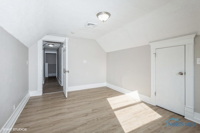 additional living space featuring lofted ceiling, a textured ceiling, and light hardwood / wood-style floors