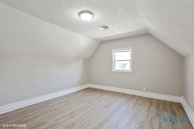 bonus room with lofted ceiling, a textured ceiling, and light hardwood / wood-style flooring