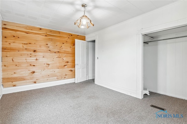 unfurnished bedroom with ornamental molding, wooden walls, a closet, and carpet